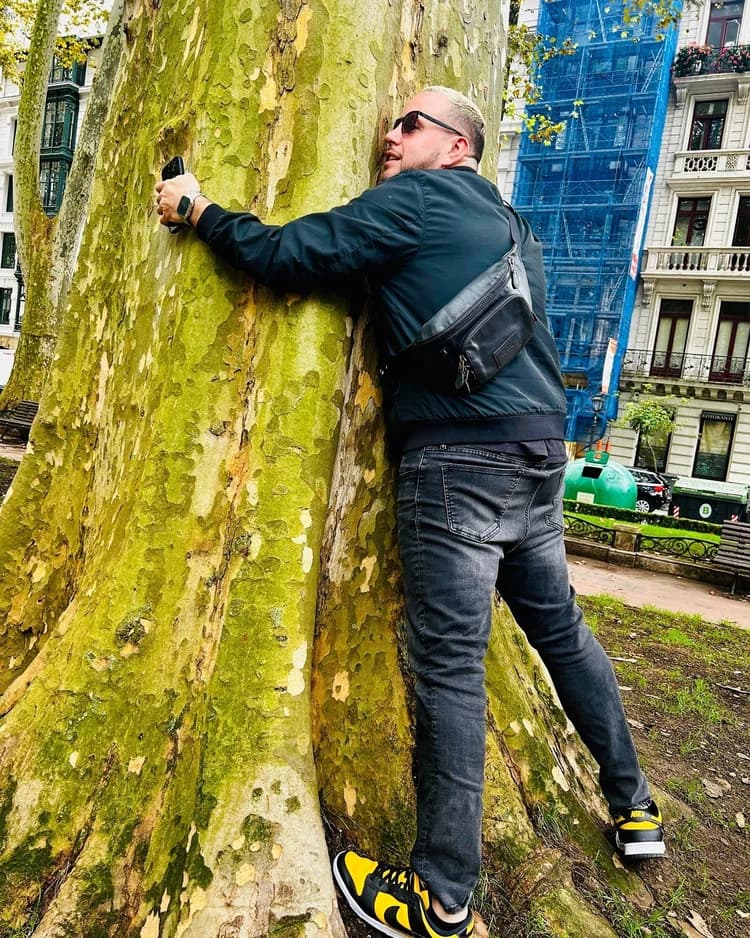 DJ Sojo playfully hugging a tree in Amsterdam